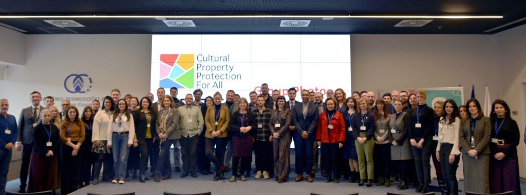 A large group of confrence attendees standing in front of a screen that says Cultural Property Proteciton for All