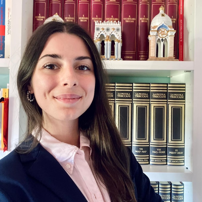 A woman in a blazer and button up shirt standing in front of a bookcase