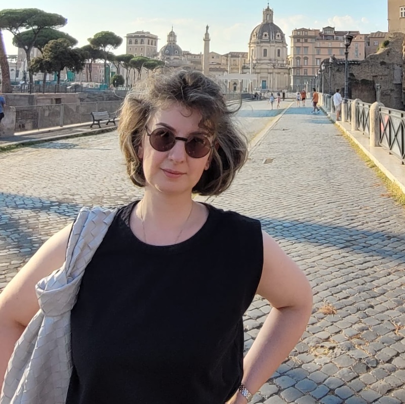 Woman in sunglasses standing on a bridge in front of historic buildings