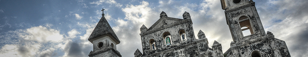 The upper towers and bell towers of a Nicaraguan church against a cloudy sky.