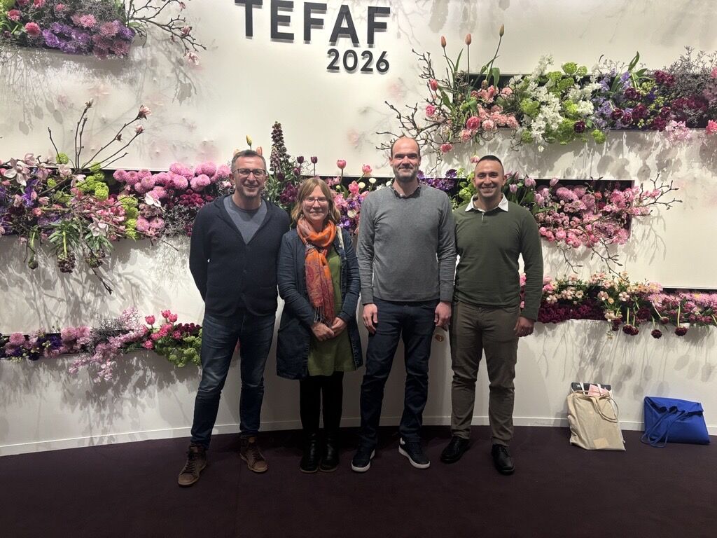 One woman and three men stand before a wall that says TEFAF 2026 on it and is decorated with flowers