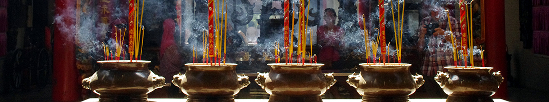 Incense sticks sticking up from 5 bowls in a line in a temple