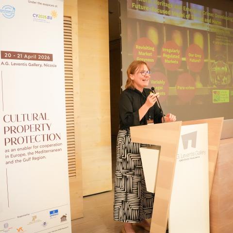 Woman standing at a conference podium speaking in front of a presentation screen.