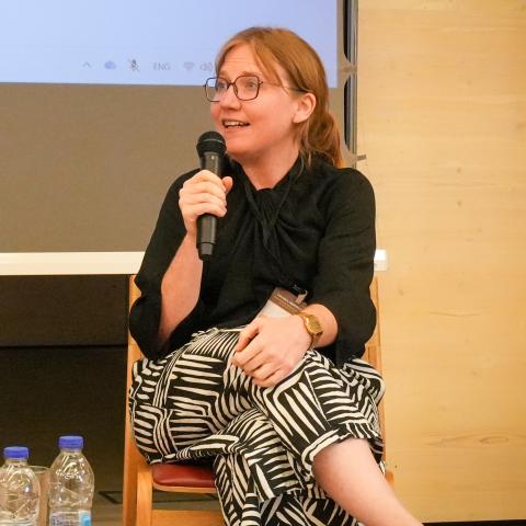 Two women in a conference panel. One holds a microphone and is speaking