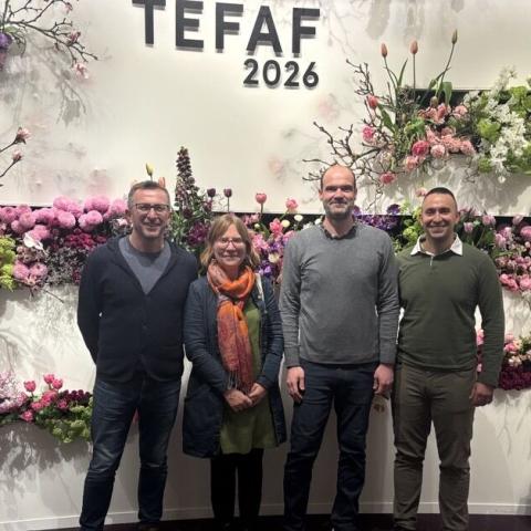 One woman and three men stand before a wall that says TEFAF 2026 on it and is decorated with flowers